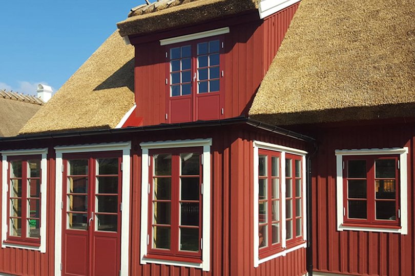 rødt to-etasjes hus med halmtak og matchende vinduer og dører